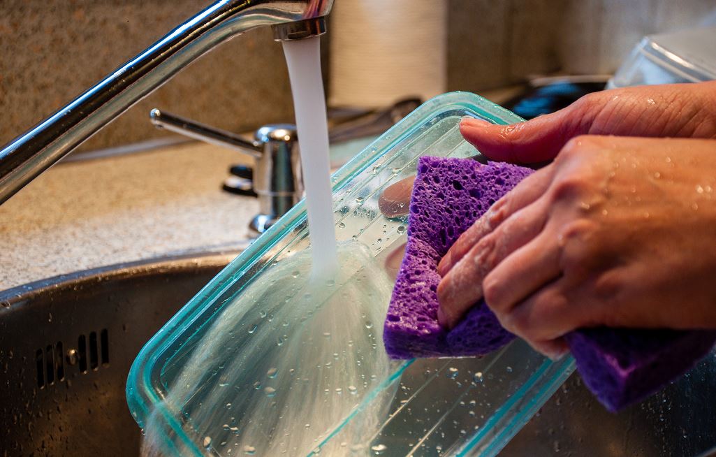 Personne Qui Nettoie Le Couvercle D'un Contenant Plastique Sous Un Robinet