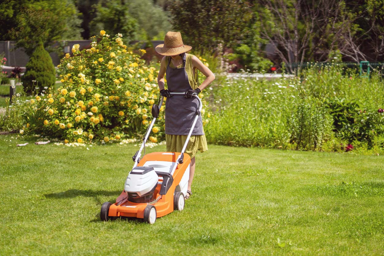 Une jeune fille en chapeau de paille tond une pelouse
